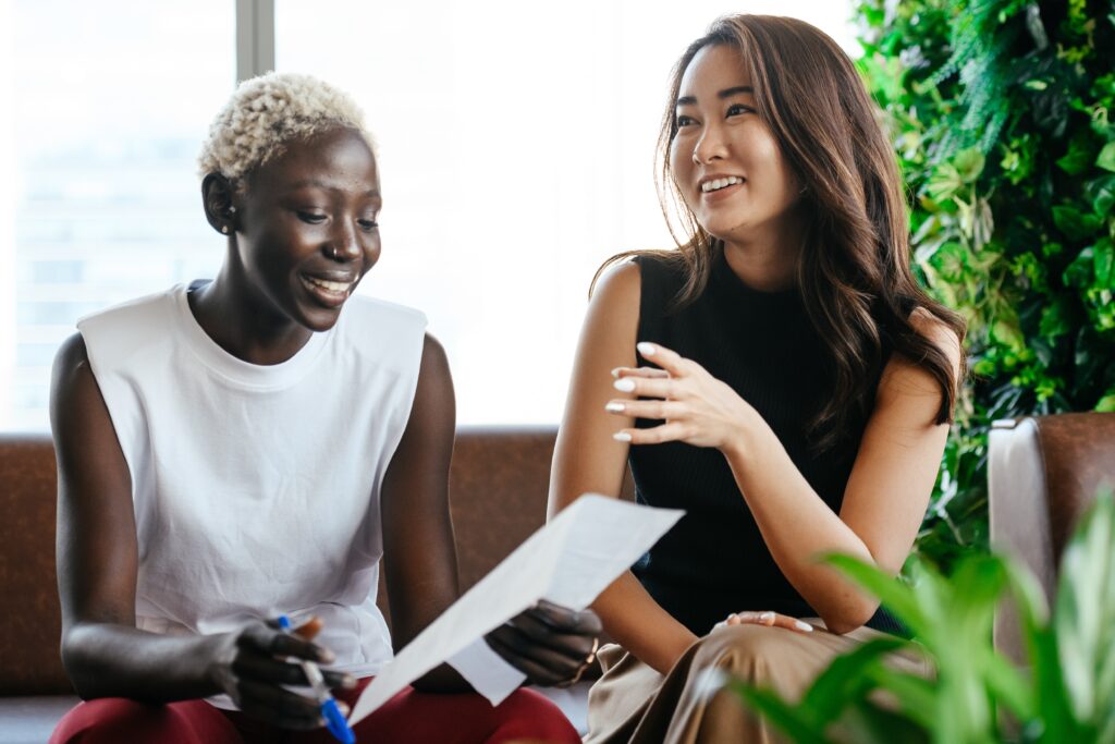 Two women smiling while working together on couch