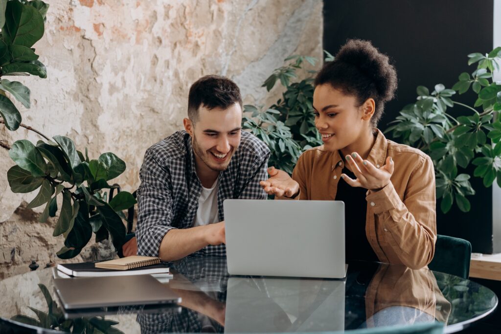 Man and woman talking and sitting next to each other at table, in front of a laptop