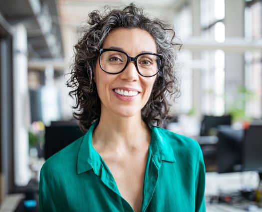 Close-up portrait of smiling mid adult businesswoman standing in office. Woman entrepreneur looking at camera and smiling